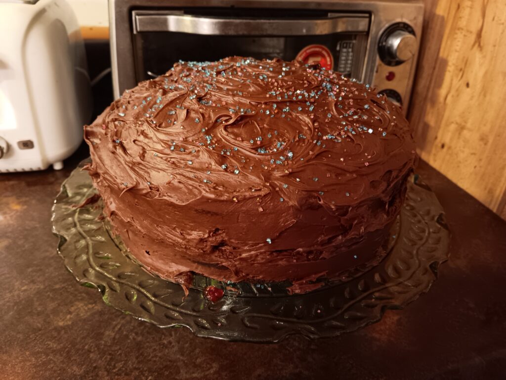 Chocolate layer cake with blue sugar sprinkles, sitting on a green glass cake stand.